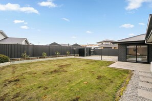 Een achtertuin met een gazon, een zwart hek en een woning met een garage.