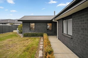 Et moderne hus i to etager med mørk murstensfacade, en synlig garageport og en velplejet græsplæne.
