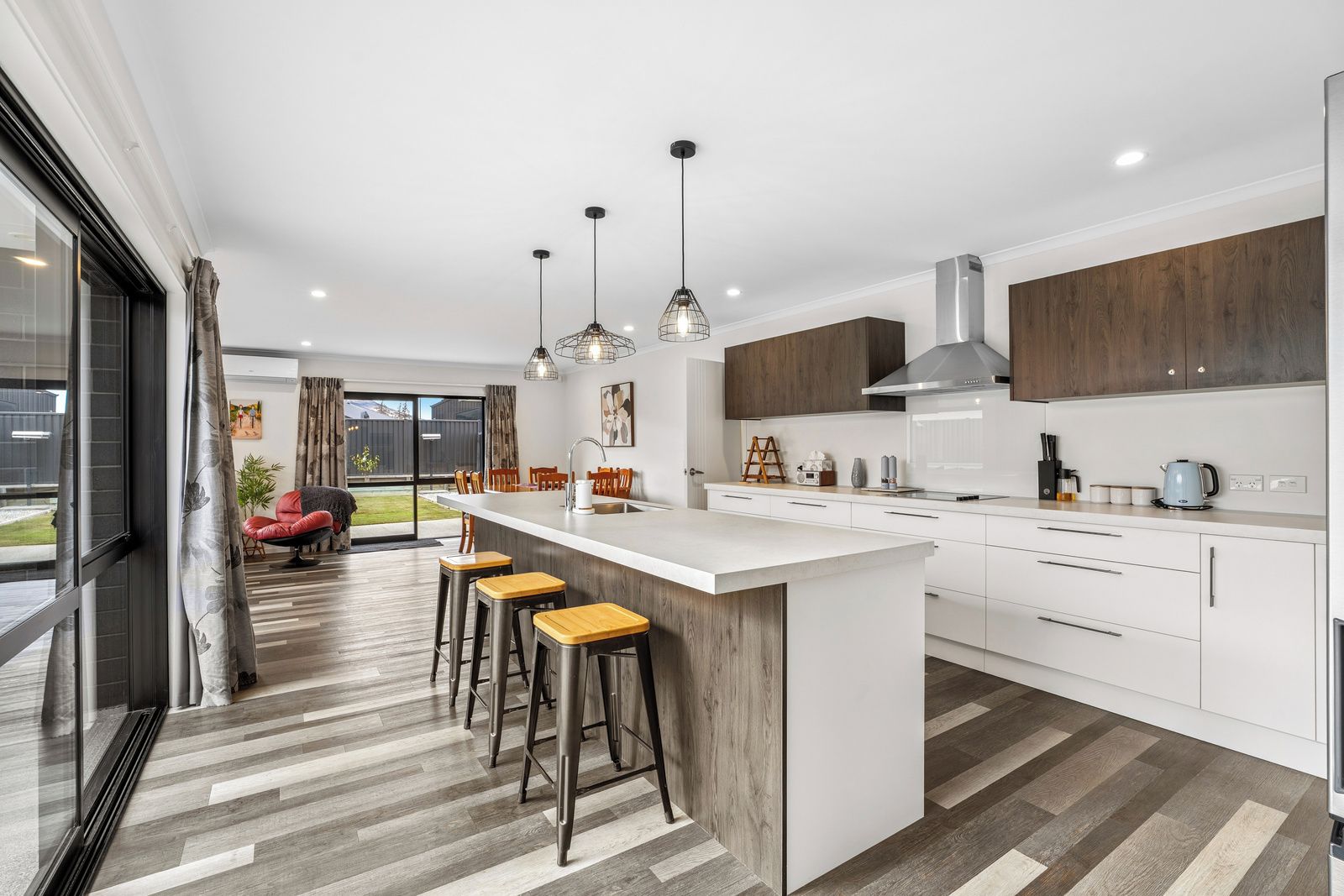 A modern kitchen with a large island, bar stools, pendant lights, and a view to the outside.