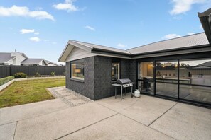 Een modern huis met een terras, een barbecue en een glazen deur die leidt naar een overdekt buitengebied.