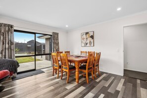 Un coin repas avec une table et des chaises en bois, une porte-fenêtre coulissante donnant sur une terrasse, et une œuvre d’art encadrée accrochée au mur.