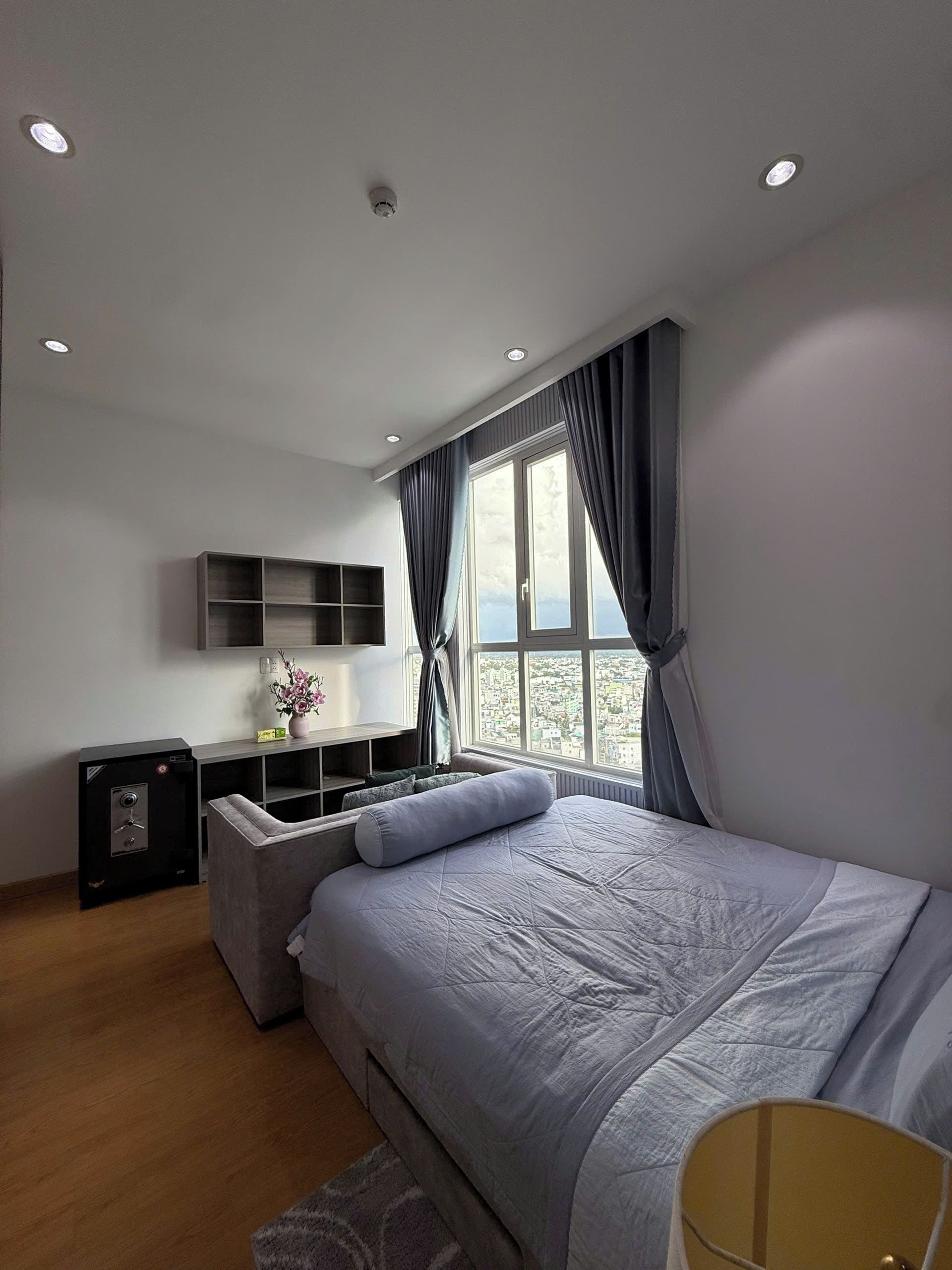 Een moderne slaapkamer met een bed, een klein bureau, een kluisje en een raam met gordijnen.