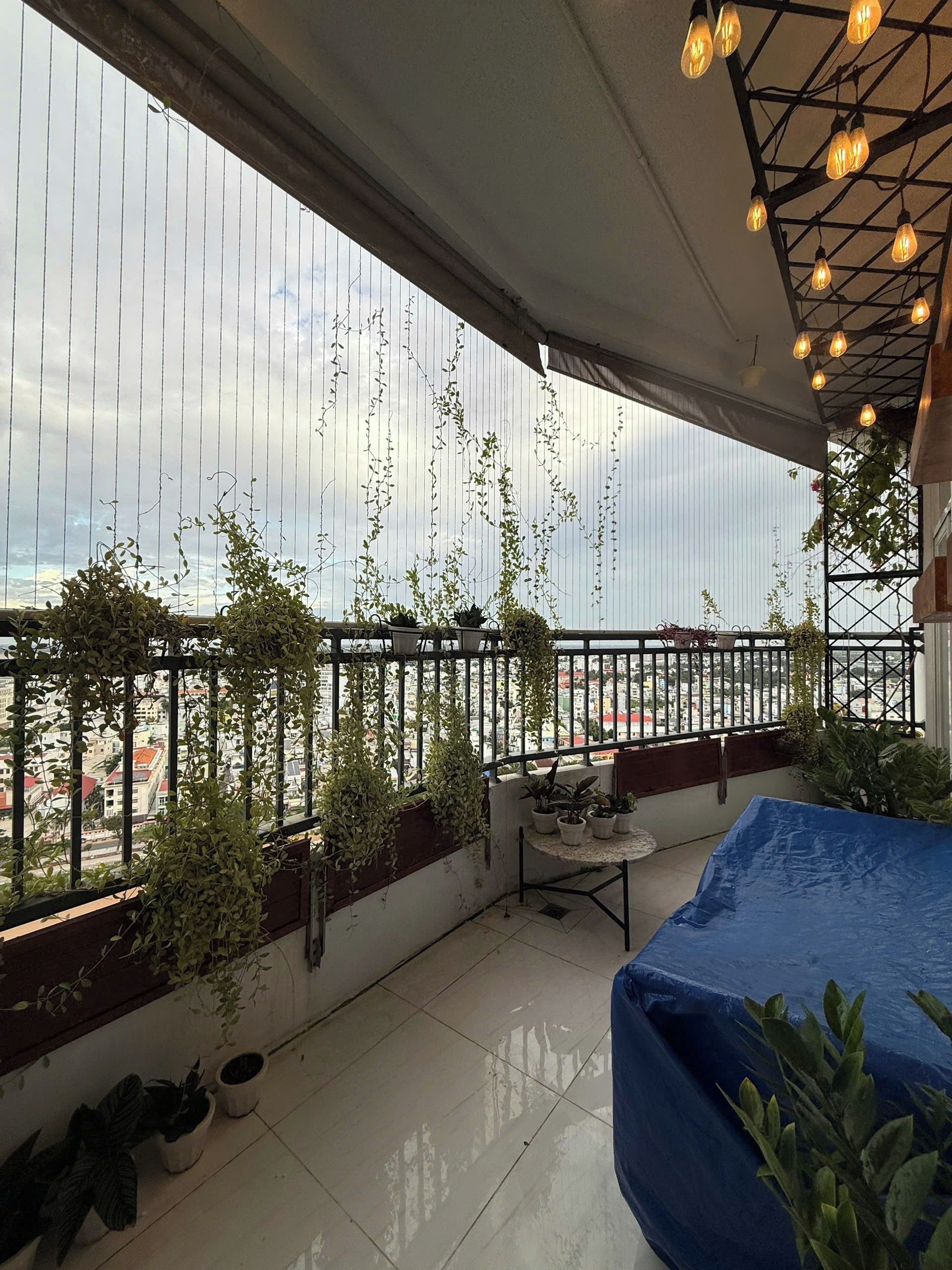 Een balkon met plantenbakken, een tafel en hanglampen.