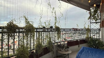 Een balkon met plantenbakken, een tafel en hanglampen.