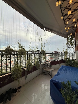A balcony with potted plants, a table, and hanging lights.