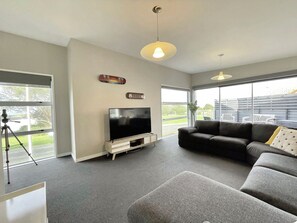 A modern living room with a flat-screen TV, a sofa, and a large window offering a view of the outdoors.