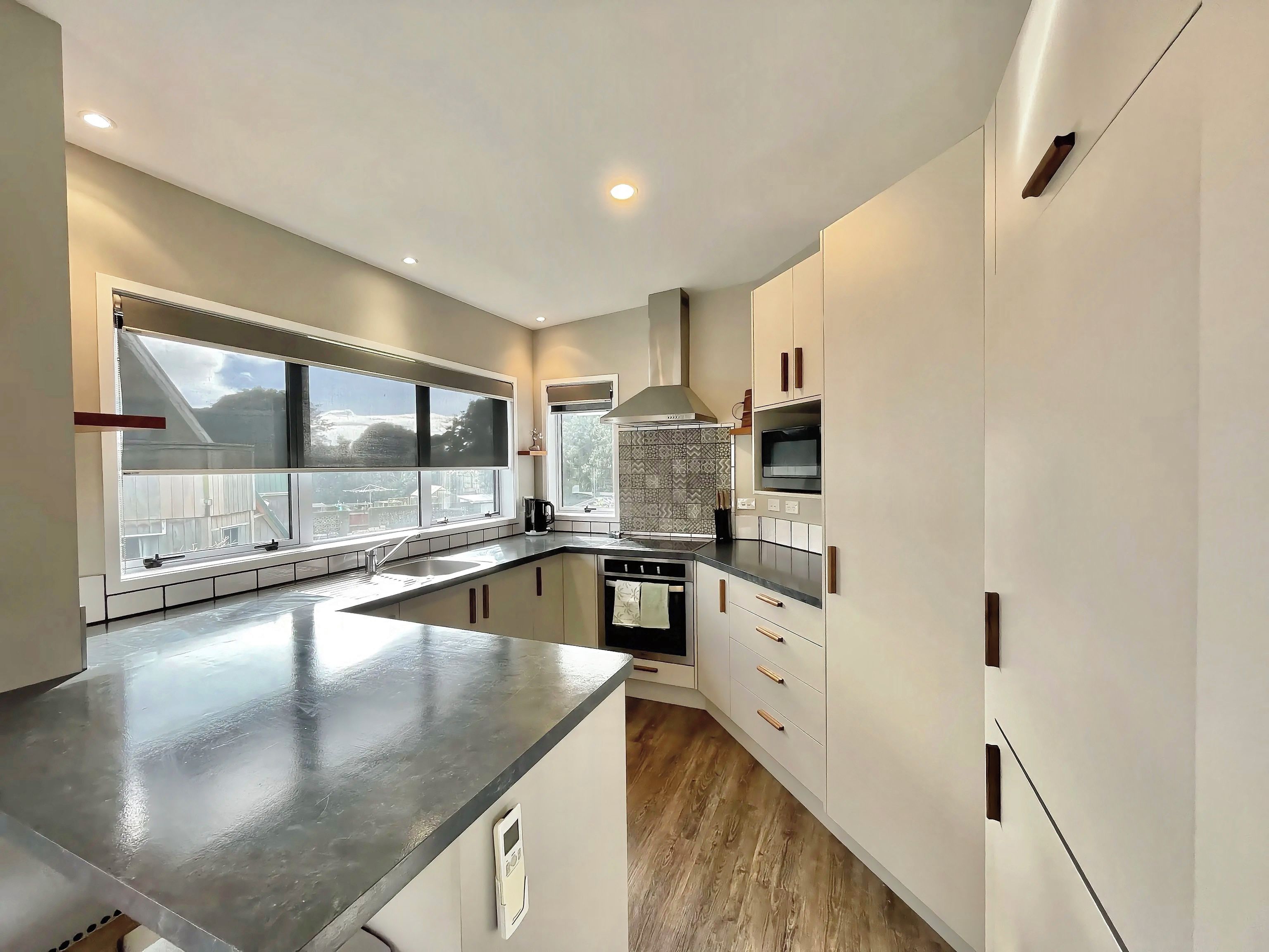 A modern kitchen with a large island, built-in oven, and a view through the windows.
