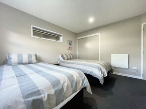 A bedroom with two beds, a window, a door, and a wall-mounted power outlet.