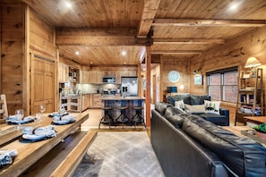 A wooden cabin interior with a kitchen, dining area, and living room. - Indoor Pool, Hot Tub & Game Room | Mountain Views, Minutes from Gatlinburg (Gatlinburg)