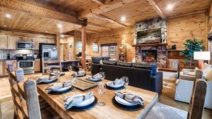 Un intérieur spacieux en bois, comprenant un coin repas aménagé pour six personnes, une cheminée et un coin salon confortable.