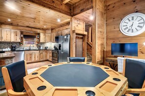 A wooden interior with a round table and chairs, a kitchen area with cabinets and appliances, and a wall clock. - Indoor Pool, Hot Tub & Game Room | Mountain Views, Minutes from Gatlinburg (Gatlinburg)