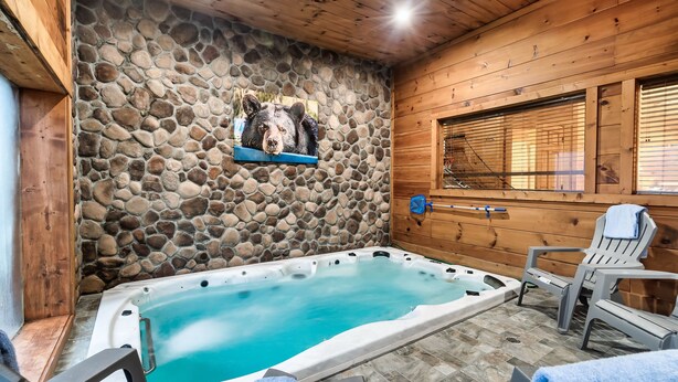 Un espace avec un bain à remous, doté d’un mur en pierre, d’un plafond en bois et de deux chaises avec des serviettes.