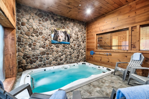 Een hoek met een bubbelbad, een stenen muur, een houten plafond en twee stoelen met handdoeken.