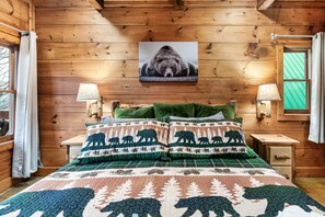 A wooden cabin bedroom with a bed, two bedside lamps, a green pillow, and a bear-themed quilt. - Indoor Pool, Hot Tub & Game Room, Mountain Views, Minutes from Gatlinburg (Gatlinburg)