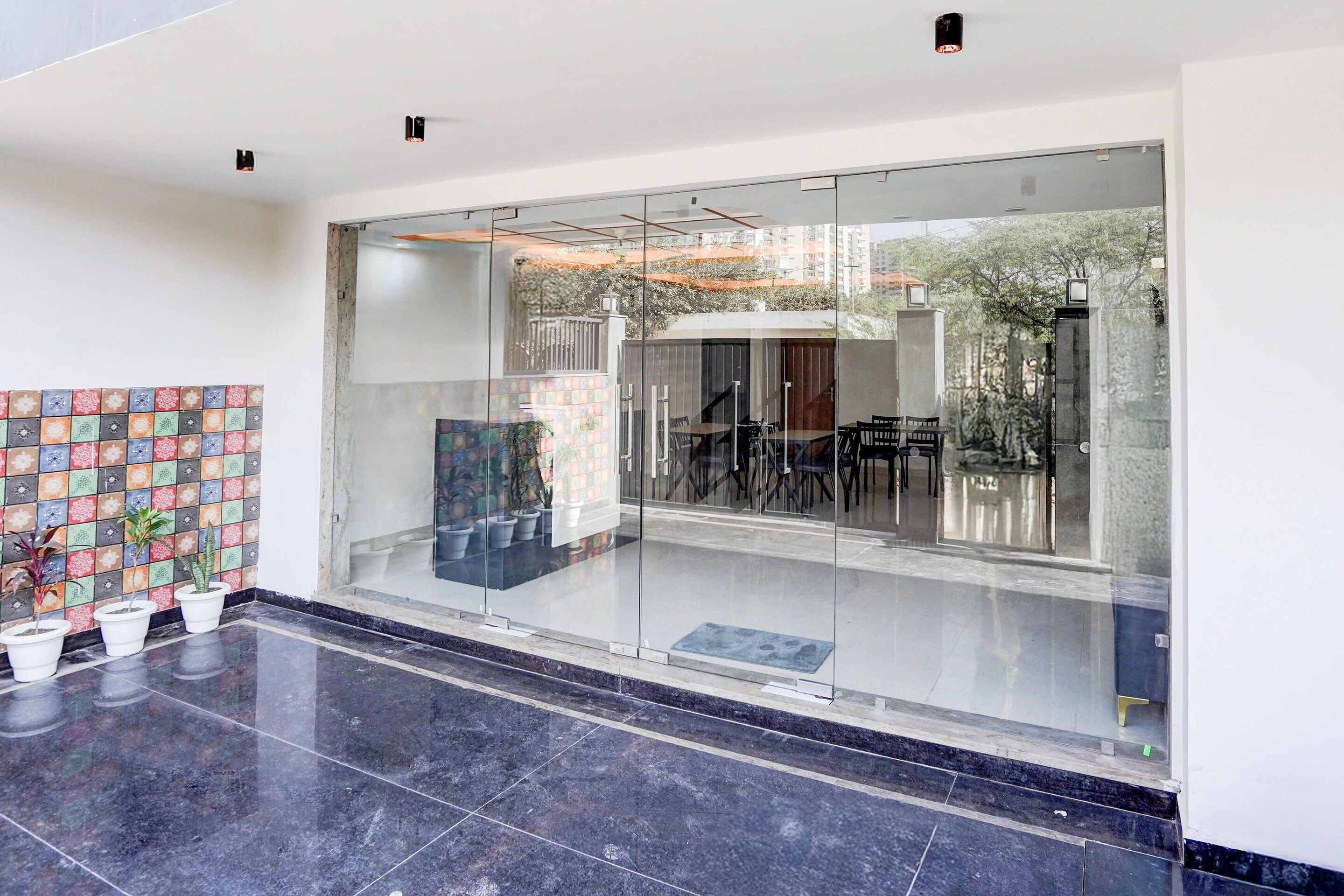 A modern interior with a glass entrance, a tiled wall with a floral pattern, and potted plants.