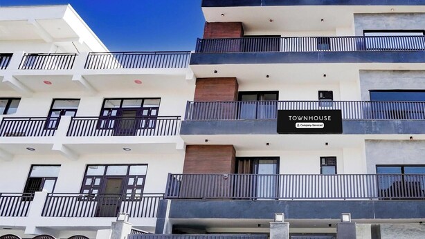 A multi-story residential building with balconies, a gated entrance, and a sign indicating it is a company-serviced townhouse. - Premium Townhouse Sector 143b (Noida)