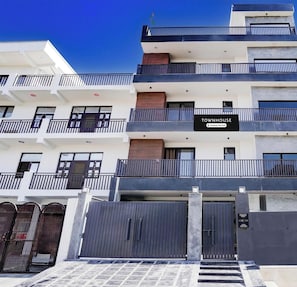 A multi-story residential building with balconies, a gated entrance, and a sign indicating it is a company-serviced townhouse. - Premium Townhouse Sector 143b (Noida)