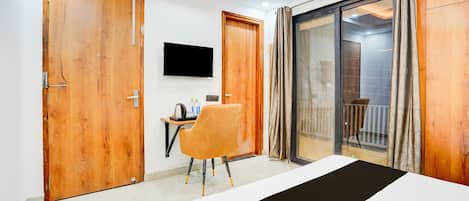 Habitación de hotel con cama, escritorio con silla, televisor y puerta corrediza de vidrio que da a un balcón.
