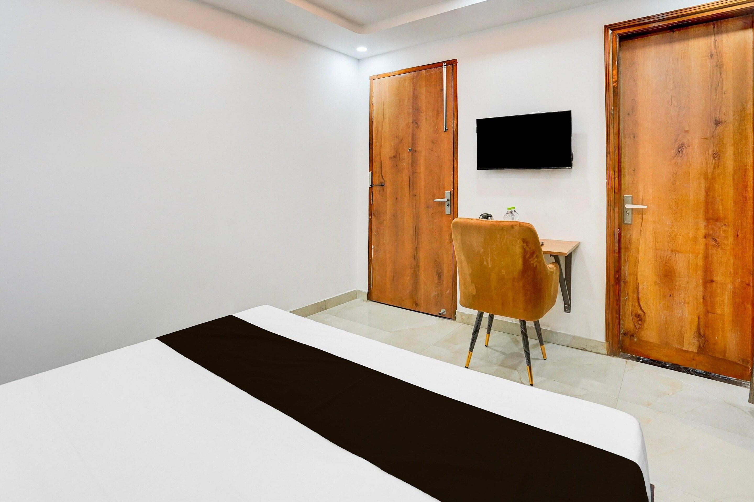 Ein Hotelzimmer mit einem Bett, einem Schreibtisch, einem Sessel und einem an der Wand befestigten Fernseher.
