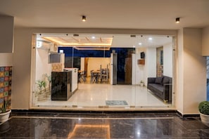 A modern interior with a glass entrance, a dining area with chairs and a table, and a sofa. - Premium Townhouse Sector 143b (Noida)