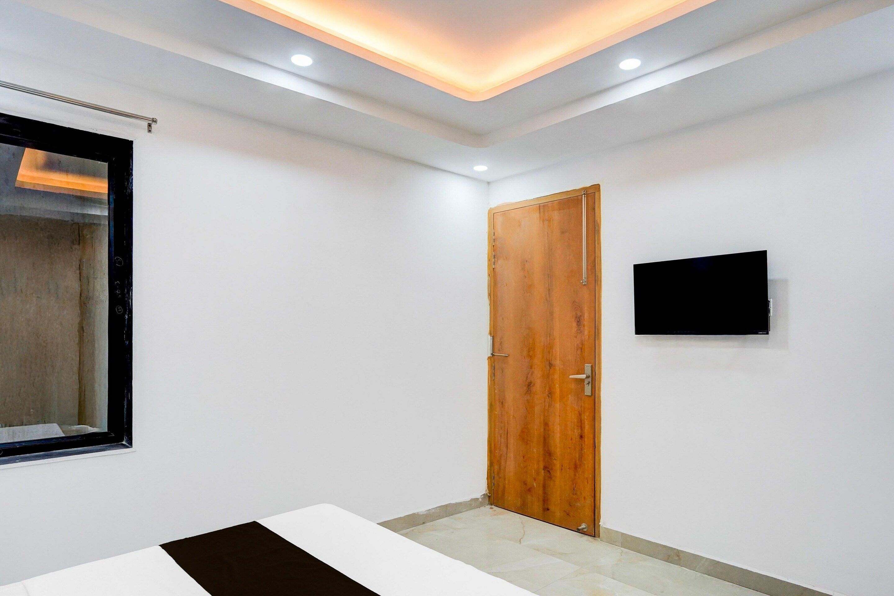 Une pièce dotée d’une porte en bois, d’un téléviseur à écran plat fixé au mur et d’une fenêtre avec des stores.