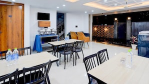 A modern dining area with tables and chairs, a television mounted on the wall, and a staircase leading to an upper level. - Premium Townhouse Sector 143b (Noida)