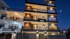 A multi-story building with balconies, a sign indicating 'Townhouse & Company Services,' and a gated entrance. - Premium Townhouse Sector 143b (Noida)