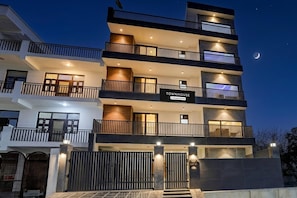 A multi-story building with balconies, a sign indicating 'Townhouse & Company Services,' and a gated entrance. - Premium Townhouse Sector 143b (Noida)