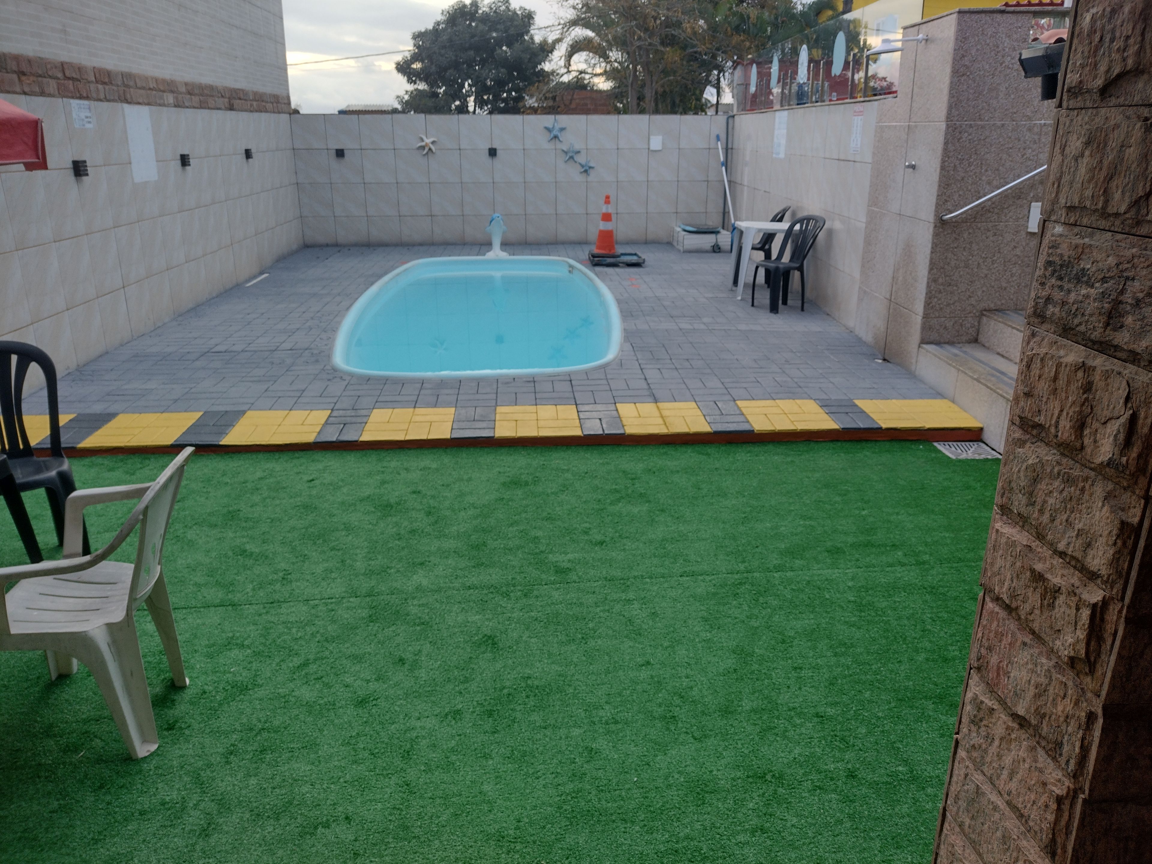 A swimming pool with a tiled deck, surrounded by a grassy area and a brick wall.