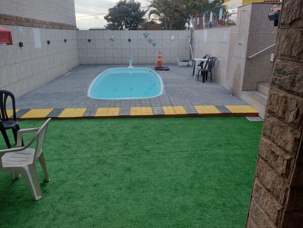 A swimming pool with a tiled deck, surrounded by a grassy area and a brick wall.