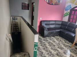 Quarto com sofá de couro preto, piso ladrilhado e escada com faixa branca e verde.