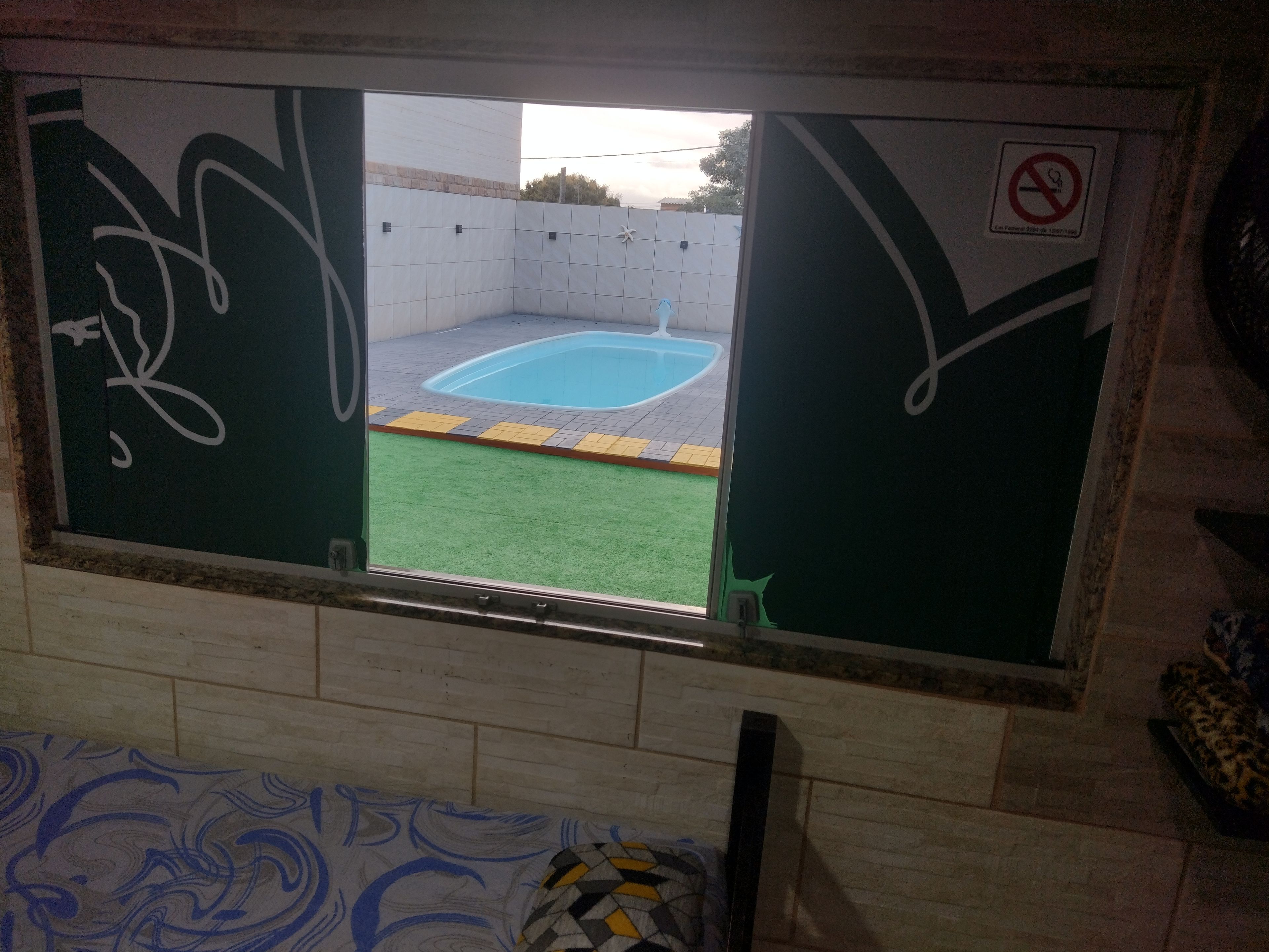 Ventana con vista a una piscina, un cartel de prohibido fumar y una zona de césped artificial verde.