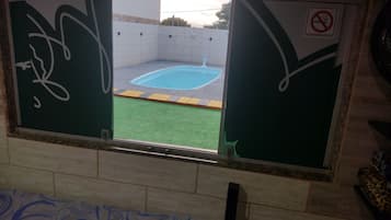 Ventana con vista a una piscina, un cartel de prohibido fumar y una zona de césped artificial verde.