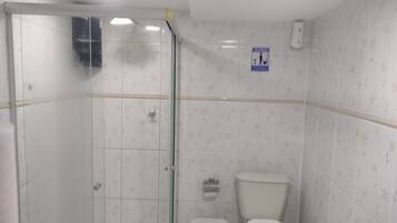 A bathroom with a glass-enclosed shower, a toilet, and a wall-mounted toilet paper holder.