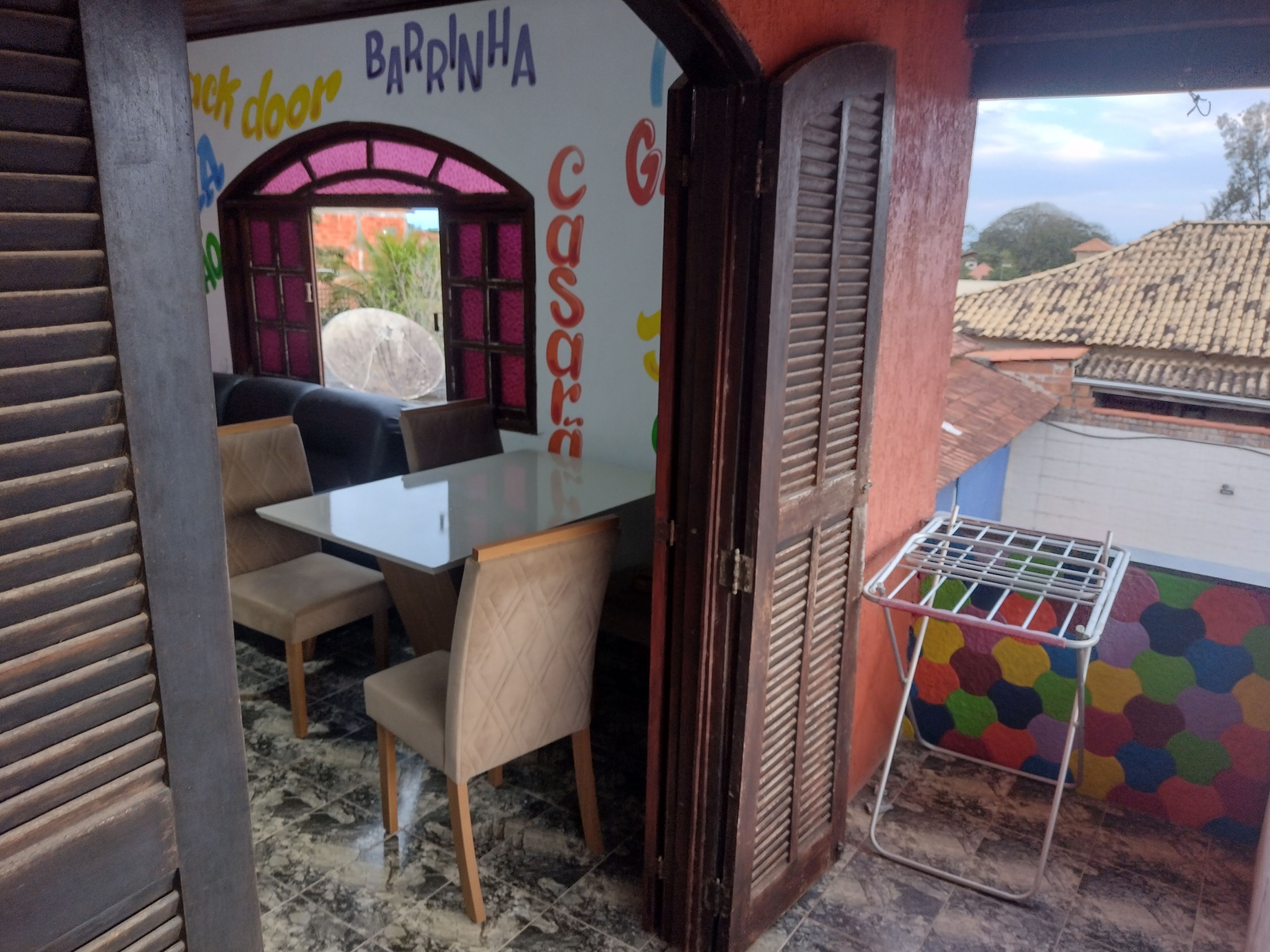 Un pequeño comedor con una mesa y sillas, una ventana con contraventanas y un mural de pared colorido.