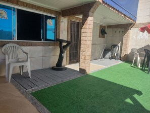 A covered outdoor seating area with artificial grass, plastic chairs, and a tree sculpture.