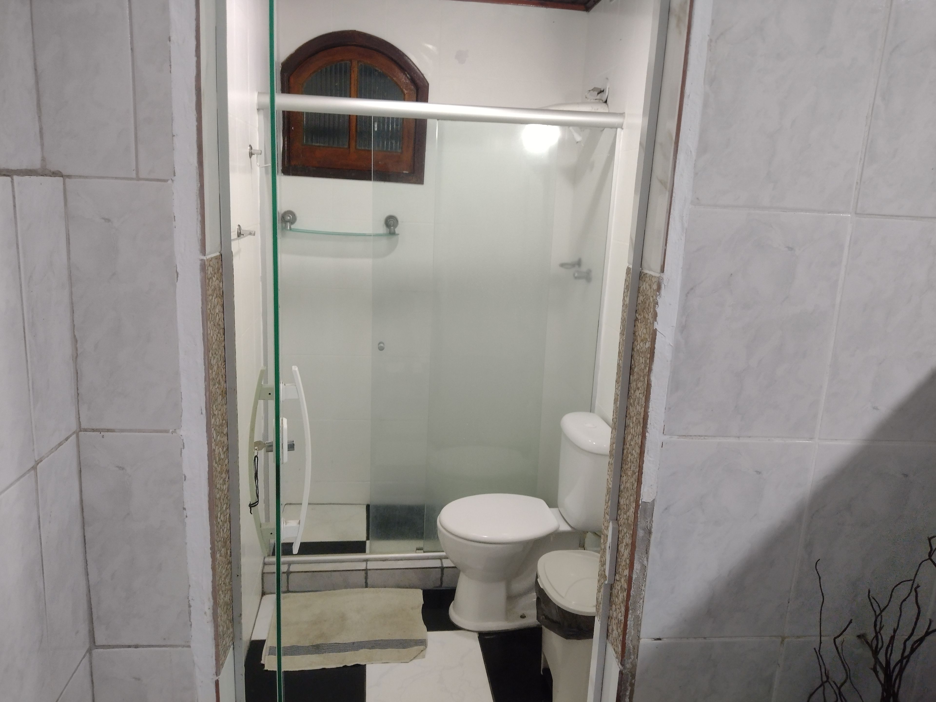 A bathroom with a glass-enclosed shower, a toilet, and a small window.