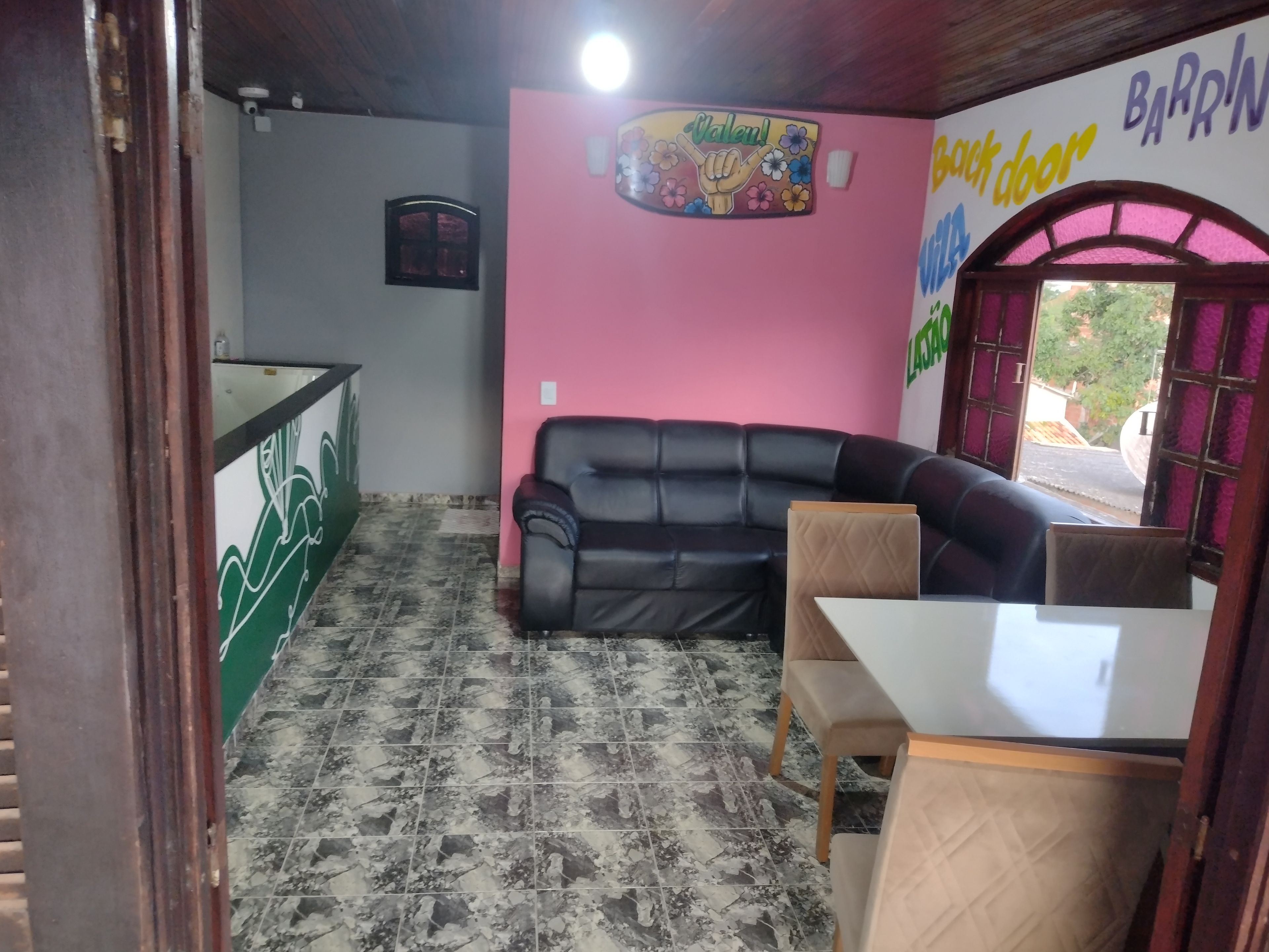 A room with a black leather sofa, a small table, a pink wall with a 'Welcome' sign, and a tiled floor.