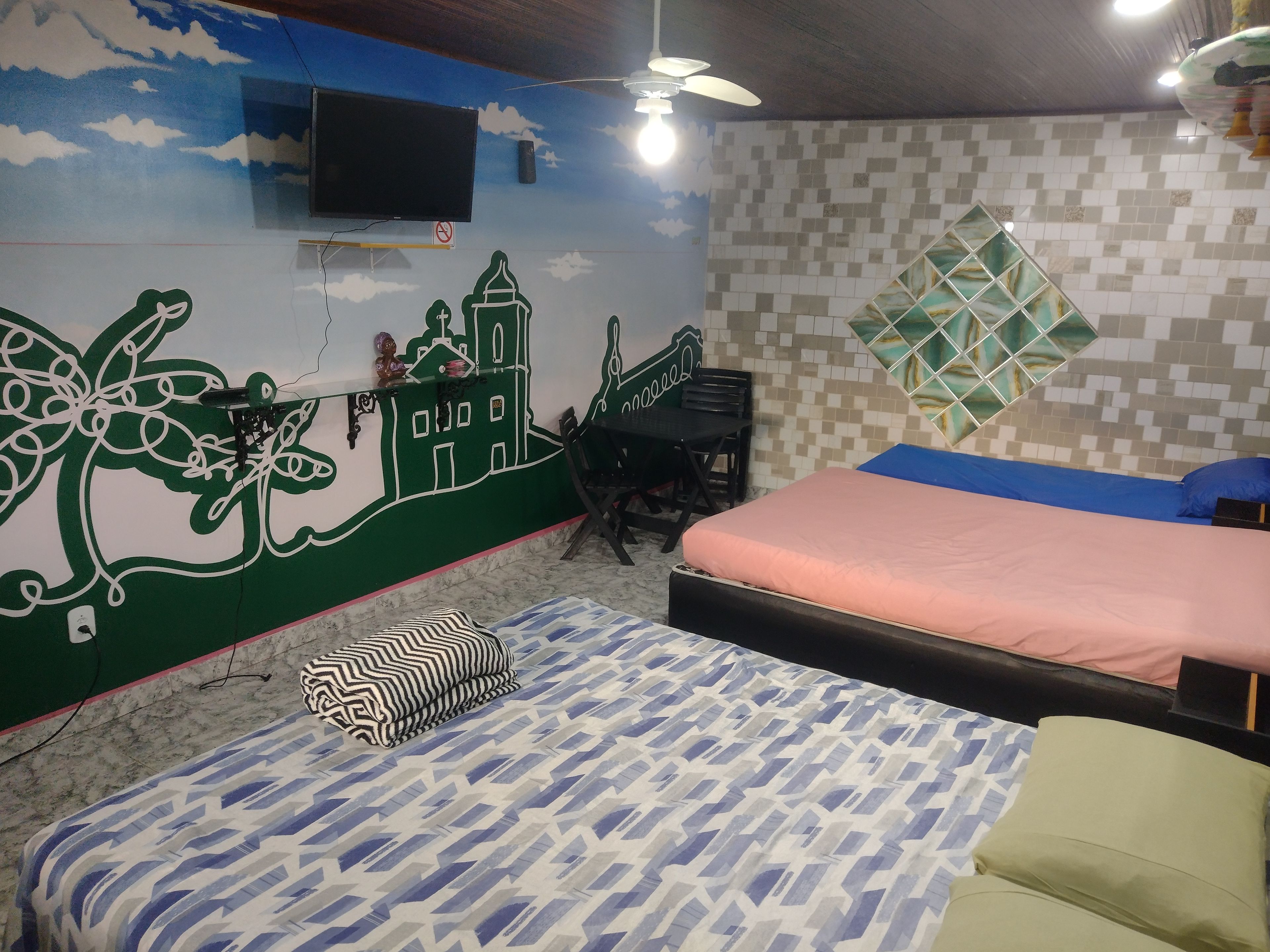 A bedroom with a bed, a desk, a chair, a television, and a ceiling fan.