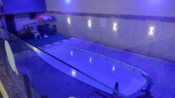 Una piscina con barrera de vidrio, pared con azulejos e iluminación, y un cartel que indica la zona de sauna.