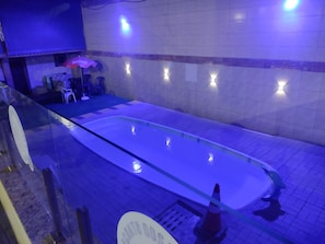 A swimming pool with a glass barrier, a tiled wall with lights, and a sign indicating a sauna area.