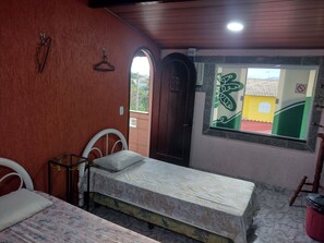 A room with a bed, a small table, a chair, a window with a view, and a door.
