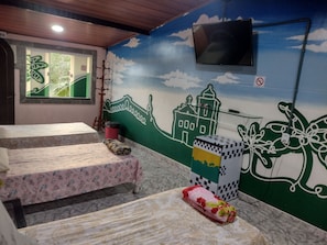 A room with two beds, a television mounted on the wall, and a mural with a cityscape. - Recanto dos Loureiros (SAQUAREMA)