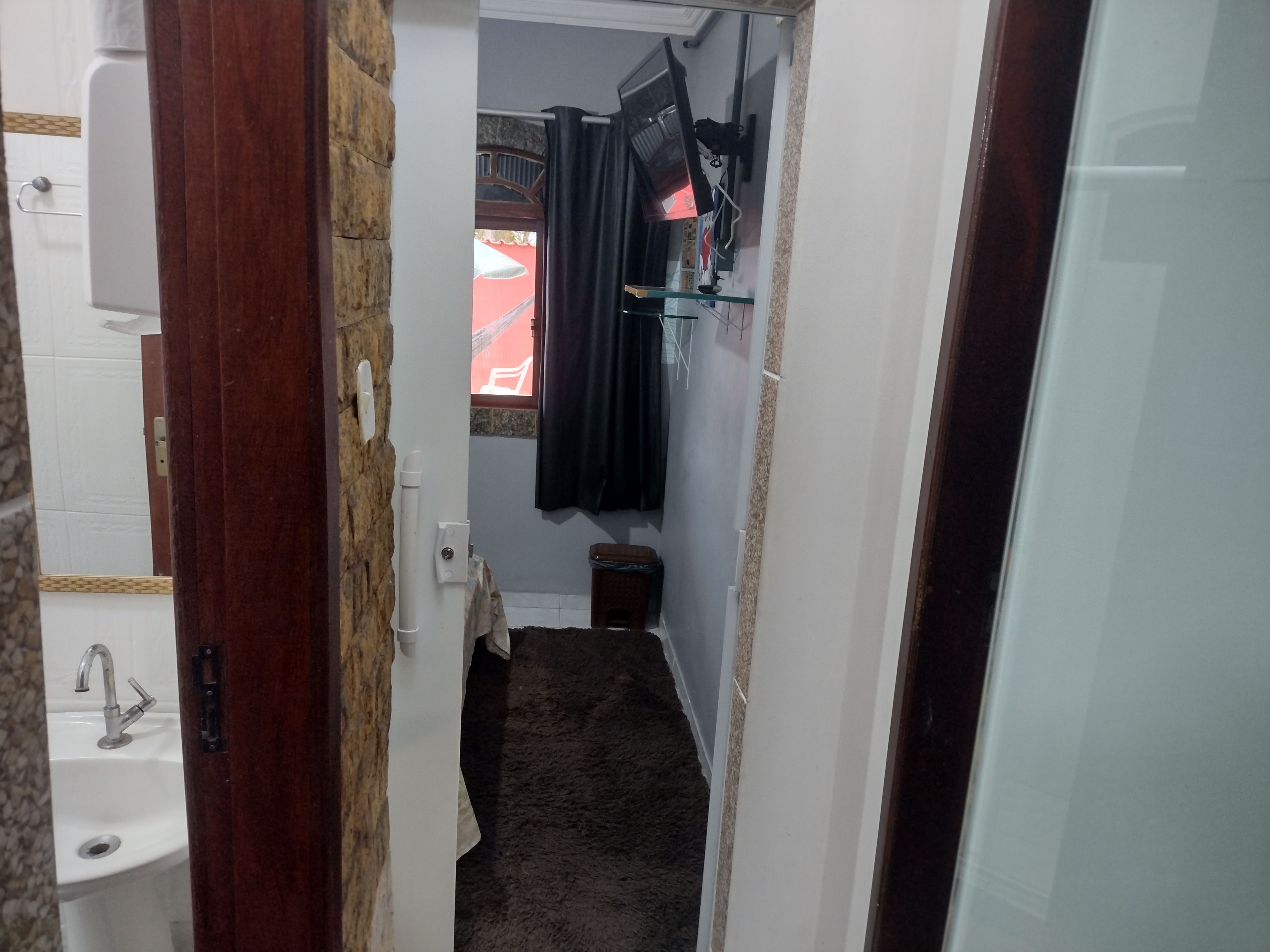 A narrow hallway with a white sink, a small wooden stool, and a dark carpeted floor.