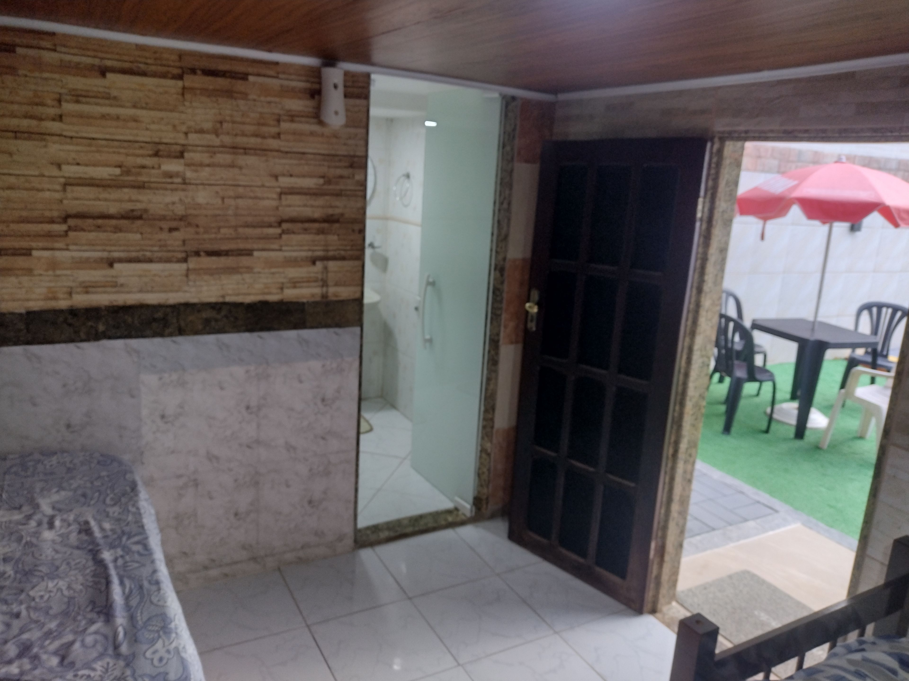 Una habitación con cama, baño con puerta de vidrio y vista a un patio exterior con sillas y sombrilla.
