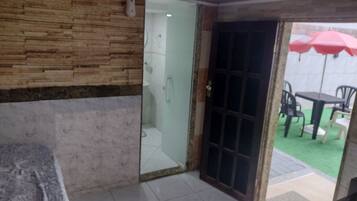 Una habitación con cama, baño con puerta de vidrio y vista a un patio exterior con sillas y sombrilla.