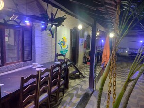 A dining area with a long table and chairs, a wall with a logo, and a patterned floor. - Recanto dos Loureiros (Saquarema)