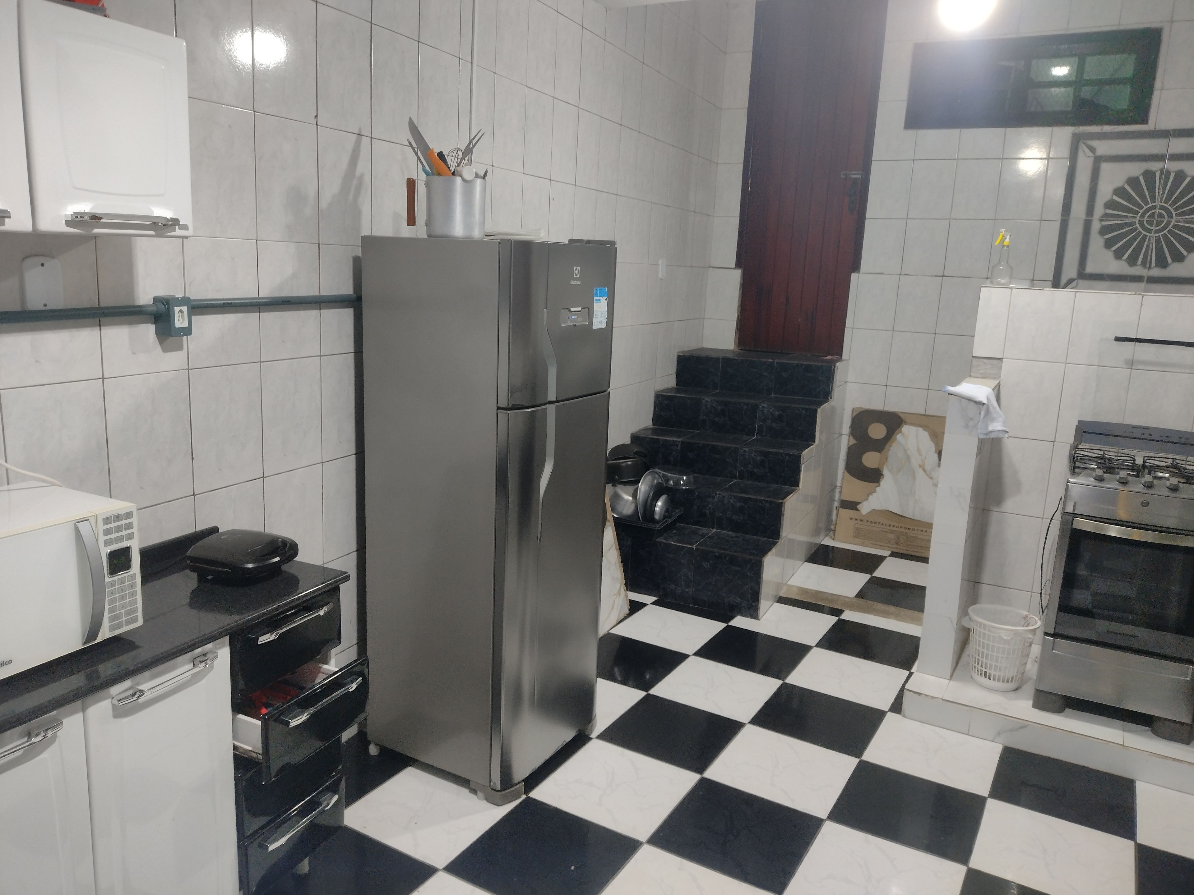 Una cocina con refrigerador, microondas, estufa y piso a cuadros blanco y negro.