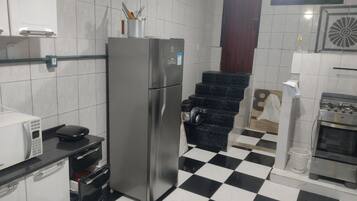 Una cocina con refrigerador, microondas, estufa y piso a cuadros blanco y negro.