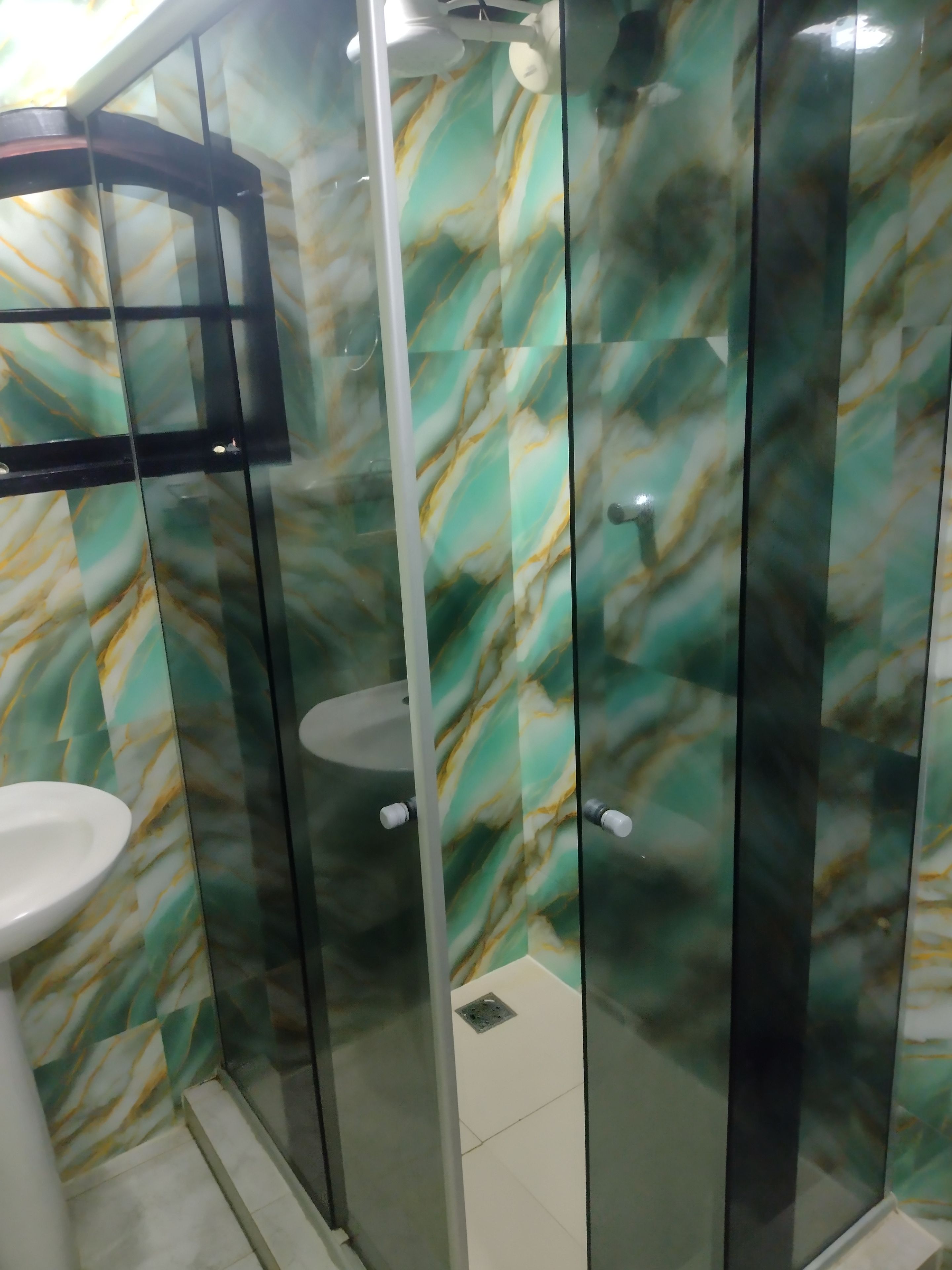 Un baño con cabina de ducha de vidrio, un lavabo blanco y una pared con diseño de mármol.